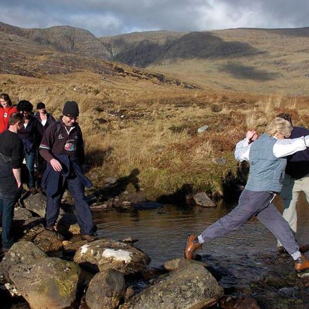 A group of people are carefully crossing a rocky stream while participating in the Sneem Walk in Ireland